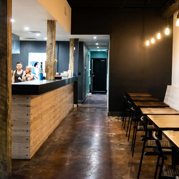 Modern restaurant interior with a long counter, open kitchen, and dining area with wooden tables and chairs.