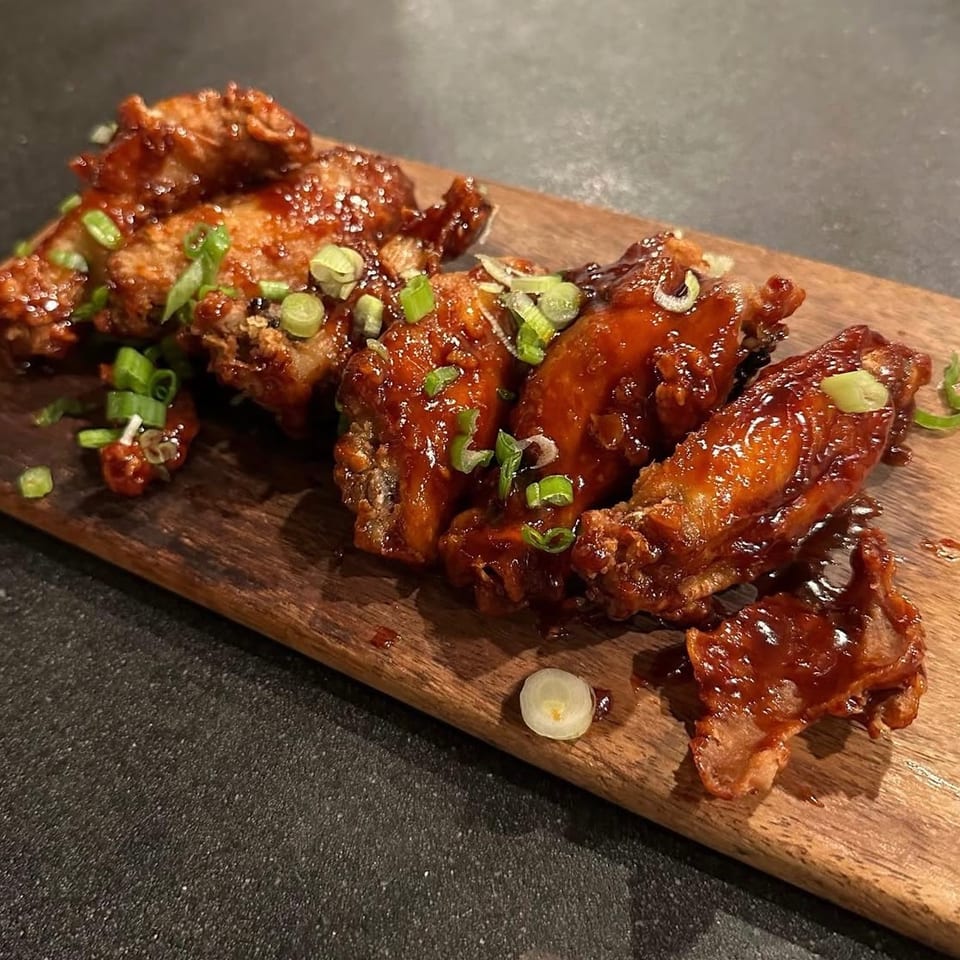 Glazed chicken wings garnished with sliced green onions, arranged on a wooden serving board.
