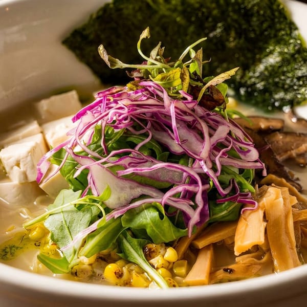 A bowl of ramen with tofu, mushrooms, corn, bamboo shoots, red cabbage, and greens.