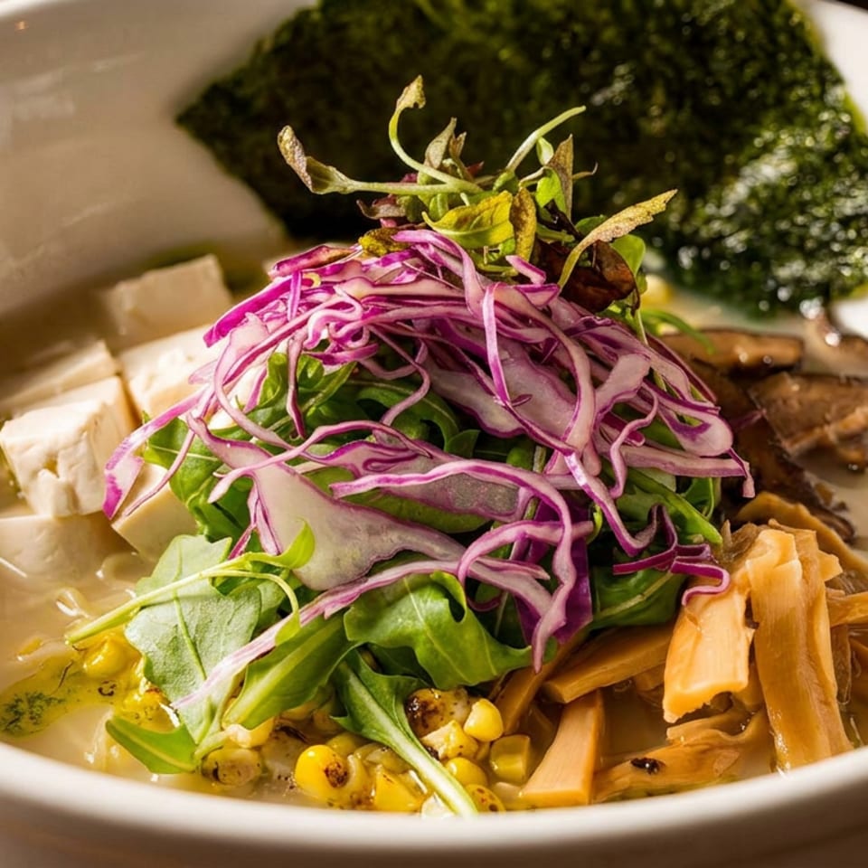 A bowl of ramen with tofu, mushrooms, corn, red cabbage, greens, and a sheet of nori.