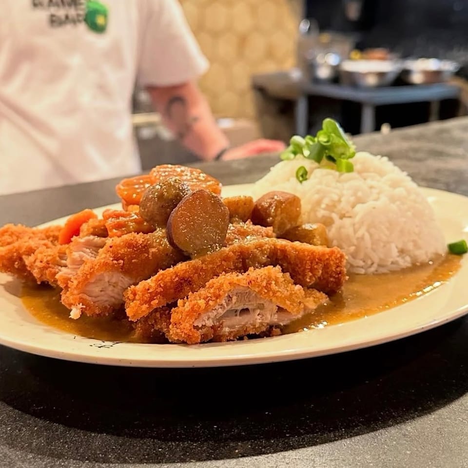 Breaded chicken cutlets with sausage, vegetables, brown gravy, and rice garnished with green onions on a restaurant plate.