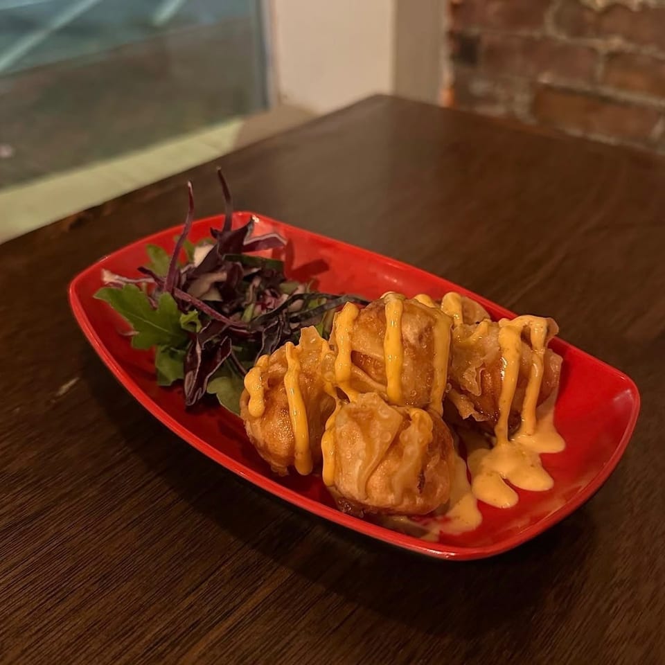 Crispy dumplings drizzled with creamy orange sauce and served with mixed greens on a red plate at a restaurant table.