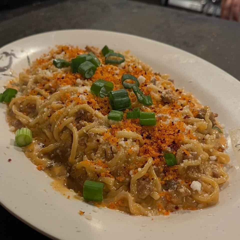 Creamy noodles with ground meat, orange breadcrumbs, grated cheese, and sliced green onions on a white plate.